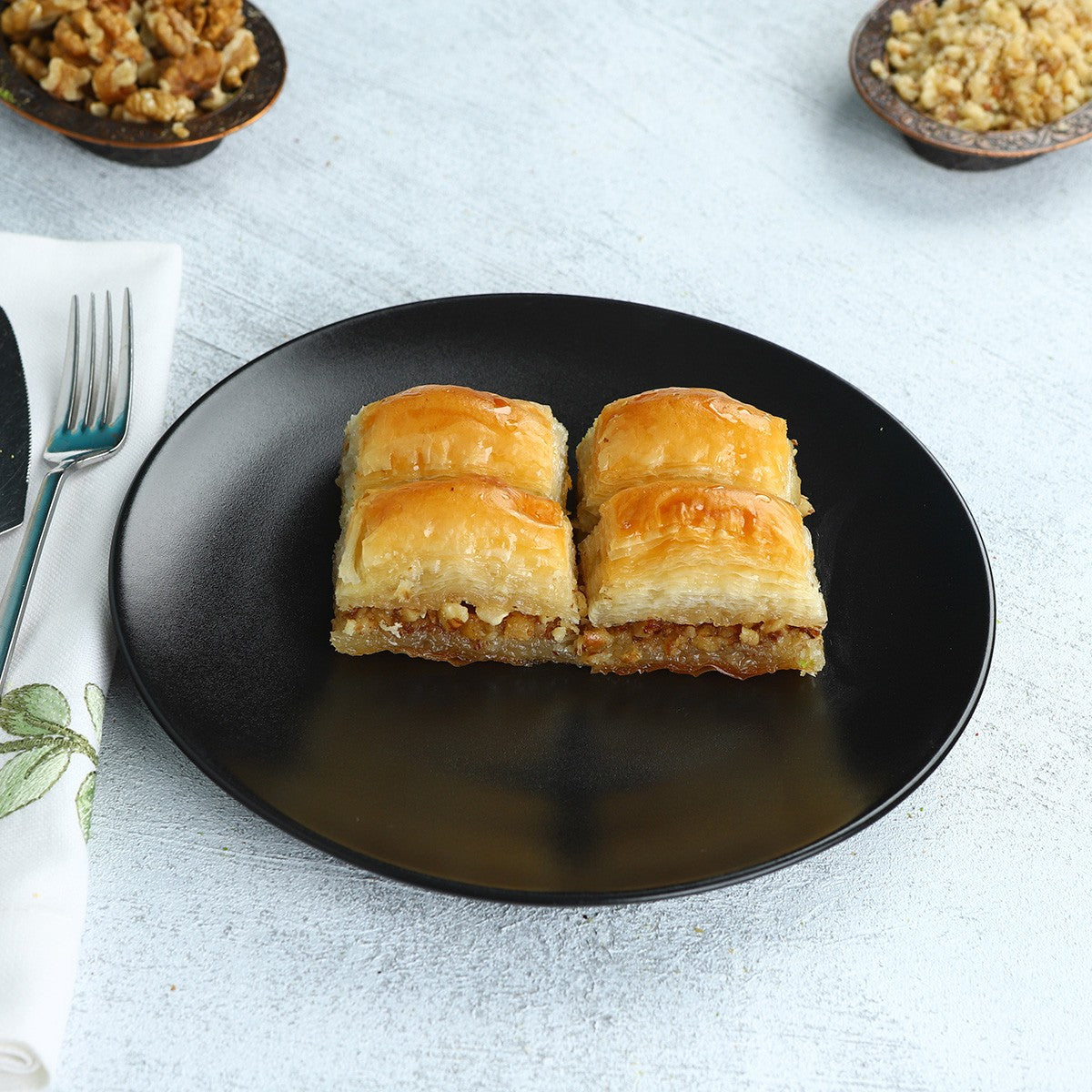 Walnut baklava pieces served on a black plate with walnuts
