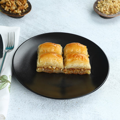 Walnut baklava pieces served on a black plate with walnuts